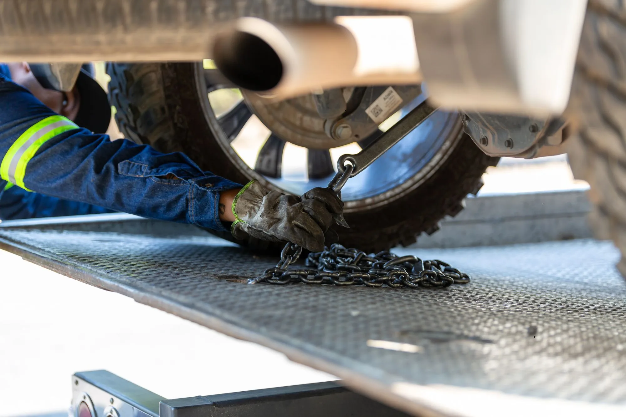 24/7 towing dispatch in De Leon Springs Tow operator in work gloves securing a wheel strap and chain on a flatbed deck